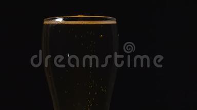 在黑色背景上的玻璃杯里放冷光啤酒。 快来点啤酒。 一杯啤酒。